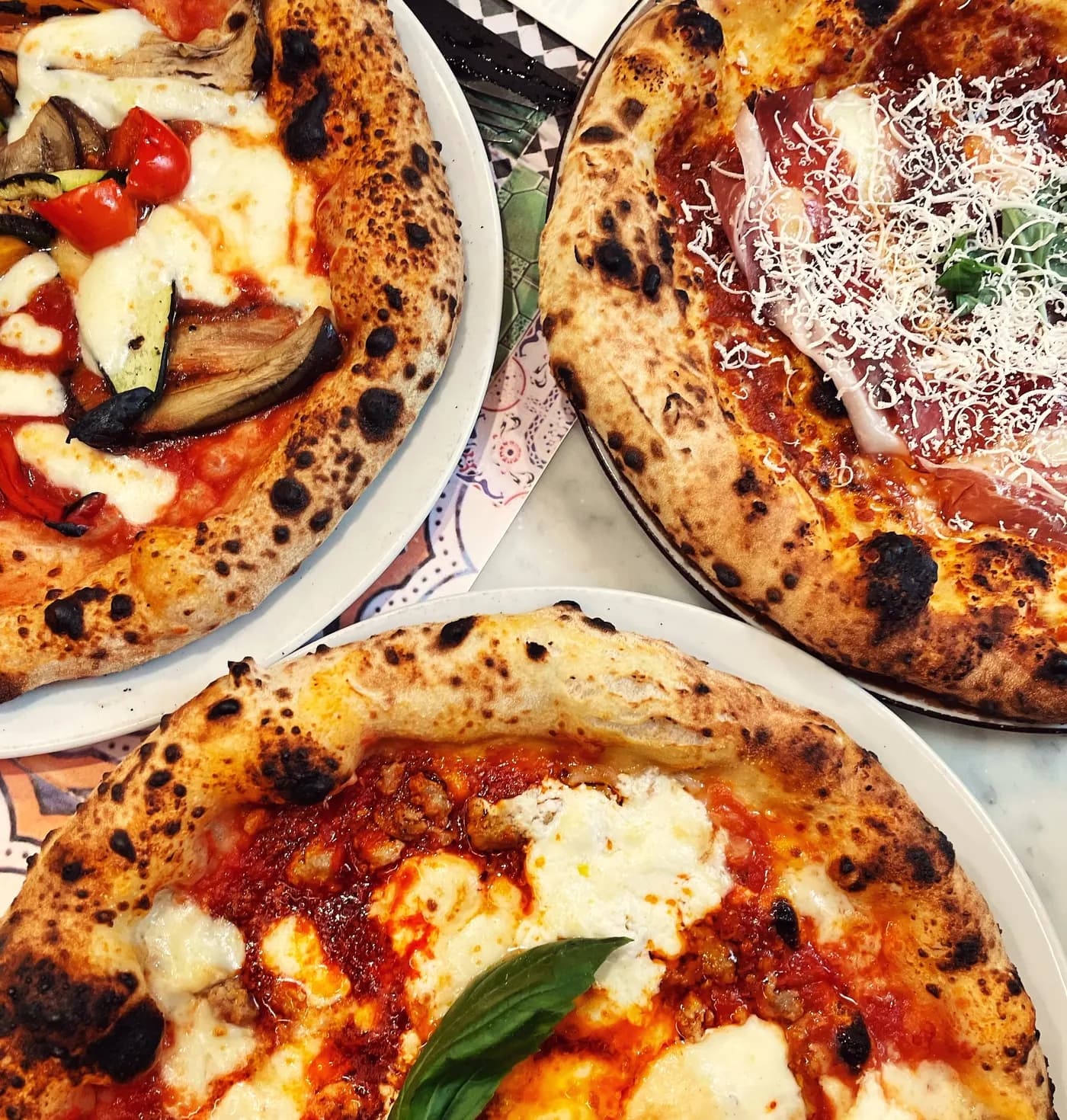 Trois pizzas type napolitaine sur une table, sorties du four