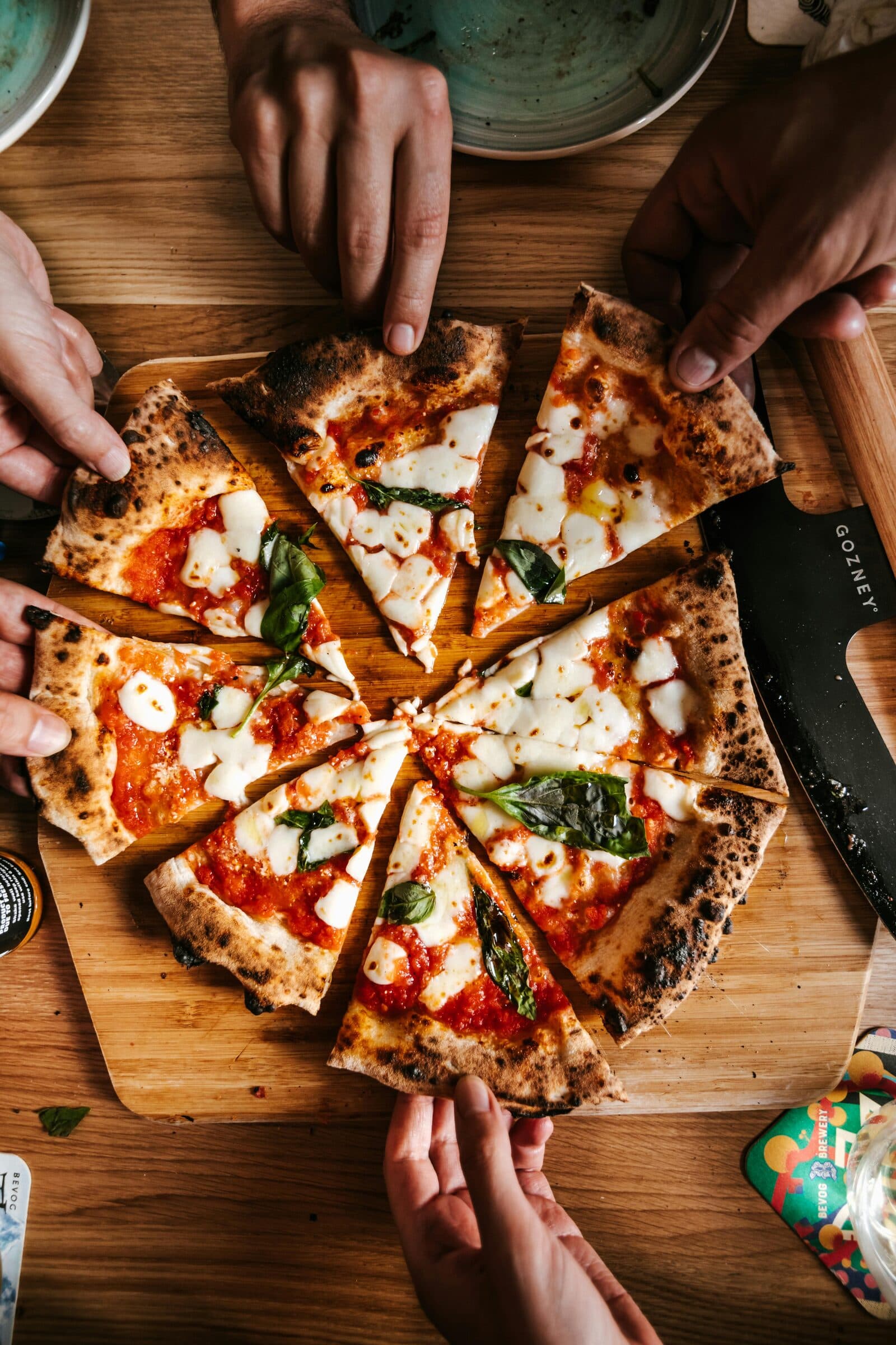 Des mains qui partagent une pizza en parts